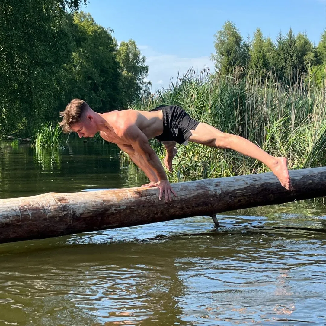 Trener warsztatów wykonuje planche na pniu drzewa nad wodą